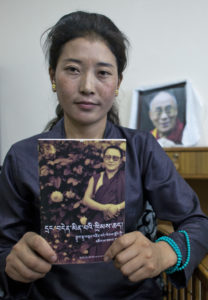 In this Wednesday, July 27, 2016 photo, Nyima Lhamo, 26, holds a book with a portrait of her uncle Tenzin Delek Rinpoche, a prominent Tibetan religious leader who died in prison last year, during an interview with the Associated Press in Dharmsala, India. She arrived in the northern hill town of Dharmsala via Nepal Sunday after two weeks on the road with the help of smugglers who she paid $9,700 for the trip, a journey she considered necessary to tell the story of her uncle to the world. The family was informed of the high priest's death in July last year and only allowed to see the body after Nyima tied a ceremonial Tibetan scarf to the bars of the prison gate and tried to hang herself. (AP Photo/Ashwini Bhatia)